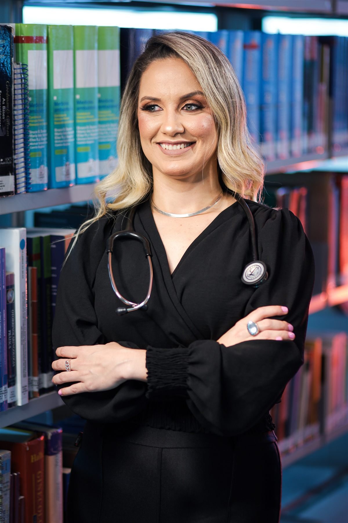 Dra. Evelyn Ferreira Alves em biblioteca médica, com estetoscópio